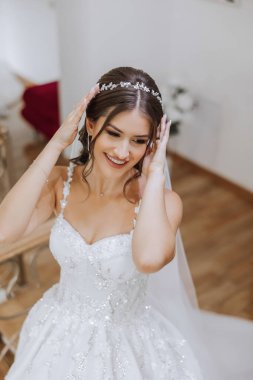 Otel odasında gelinin portresi. Güzel genç bir kız beyaz bir gelinlik giyiyor. Modern düğün saç stili. Doğal makyaj..