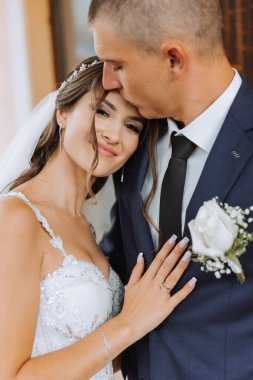 Yakışıklı bir damat, gelinini bembeyaz bir elbiseyle kucaklıyor ve güzel bir açık havada gülümsüyor. Açık gökyüzünün altında. Yüksek kalite fotoğraf. Yeni evli bir çift güneşli bir yaz gününde birlikte poz verir..