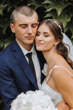 Yakışıklı bir damat, gelinini bembeyaz bir elbiseyle kucaklıyor ve güzel bir açık havada gülümsüyor. Açık gökyüzünün altında. Yüksek kalite fotoğraf. Yeni evli bir çift güneşli bir yaz gününde birlikte poz verir..