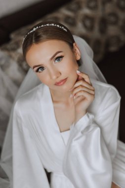 Düğün töreninden önce sabahları sabahlık giymiş güzel bir gelin. Gelinin saç stili inanılmaz. Doğal ve modern makyaj. Sabahlık giymiş genç bir gelinin portresi.