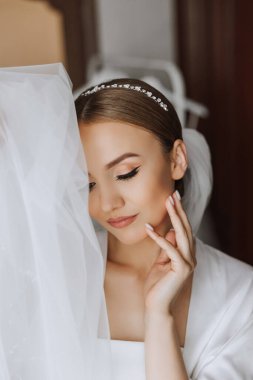 Düğün töreninden önce sabahları sabahlık giymiş güzel bir gelin. Gelinin saç stili inanılmaz. Doğal ve modern makyaj. Sabahlık giymiş genç bir gelinin portresi.