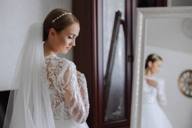 Otel odasında gelinin portresi. Güzel genç bir kız beyaz bir gelinlik giyiyor. Modern düğün saç stili. Doğal makyaj..