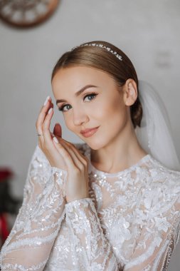 Otel odasında gelinin portresi. Güzel genç bir kız beyaz bir gelinlik giyiyor. Modern düğün saç stili. Doğal makyaj..