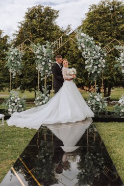 Yakışıklı bir damat, gelinini bembeyaz bir elbiseyle kucaklıyor ve güzel bir açık havada gülümsüyor. Açık gökyüzünün altında. Yüksek kalite fotoğraf. Yeni evli bir çift güneşli bir yaz gününde birlikte poz verir..