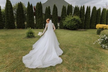 Photo from the back. A beautiful young woman in a white wedding dress is smiling on a warm wedding summer day clipart