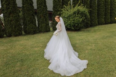 Photo from the back. A beautiful young woman in a white wedding dress is smiling on a warm wedding summer day clipart