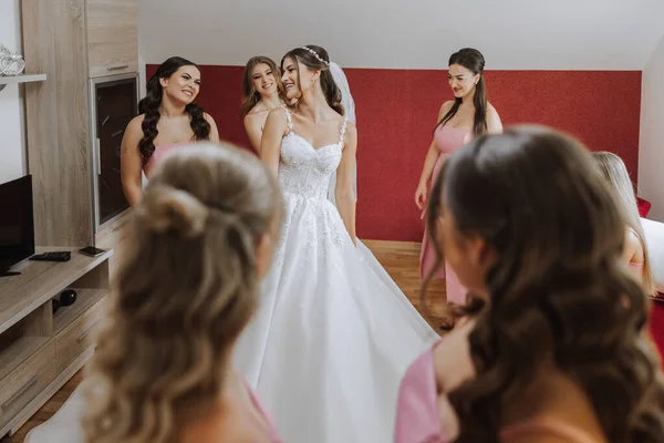 Wedding morning. Bridesmaids help put on the white wedding dress. A young woman is preparing to meet her groom and having fun with her friends