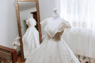 Yatak odasının içinde tören için hazırlanmış gelinlik var. Bir otel odasında, bir mankenin üzerinde güzel, gür bir gelinlik..