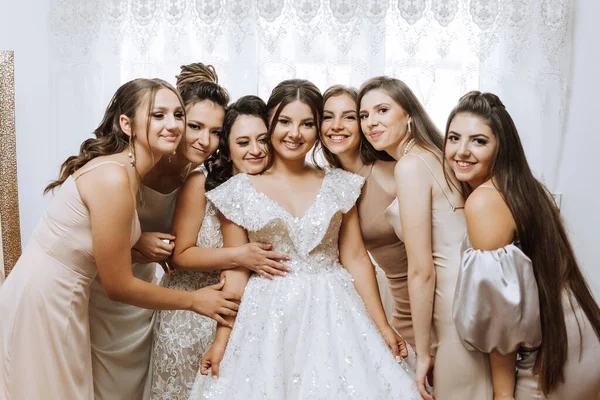 Portrait of the bride with her friends. Elegant and stylish bride with her friends in matching dresses in the room in the morning. Many beautiful girls in one photo.