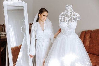 İnanılmaz güzel bir gelinin sabah hazırlığı. İçeride bir mankenin üzerinde duran gelinliğin yanında güzel bir bornoz giymiş bir kız. Gelinin düğün hazırlıkları..