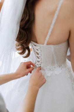 Gelinin arkadaşı sabahları beyaz bir gelinlik giymesine yardım ediyor. Düğün sabahı, bulanık odak. Gelinin bir arkadaşı gelinliğini bağlamaya yardım ediyor..