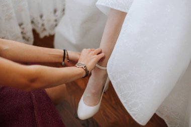 Güzel gelinlikli genç gelin içeride ayakkabı giyiyor. Gelin düğün töreninden önce ayakkabı giyer. Gelinin yüksek topuklu düğün ayakkabısı giymesinin ayrıntıları. Gelin ayakkabıları..