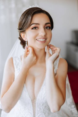 Evdeki düğün töreninden önce küpe takan genç ve güzel bir gelin. Beyaz gelinlikli bir gelin, sabahları odasına küpe takar..