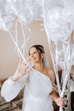 Beyaz elbiseli, bornozlu güzel esmer gelin ellerinde beyaz jel toplar ve odasında düğün gününün tadını çıkarıyor. Düğün fotoğrafçılığı.