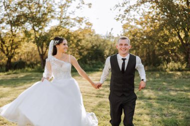 Bir düğün çifti bir sonbahar günü doğada yürüyor. Mutlu genç gelin ve zarif damat el ele tutuşuyor. Yeni evlilerin düğün gününde şık bir çift..