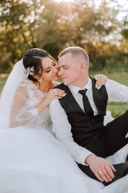 Güzel ve şık yeni evliler güzel bir bahçede sonbahar doğasının arka planına karşı sarılıp gülümsüyorlar. İnanılmaz güzel genç bir gelin, sevgili damadının omzuna yaslandı.