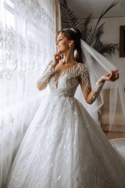 Şık bir gelinlik içinde siyah saçlı ve düğün sabahı odasında çarpıcı makyajlı güzel bir gelinin moda fotoğrafı. Gelin düğün için hazırlanıyor.