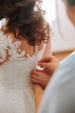 Gelinin arkadaşı sabahları beyaz bir gelinlik giymesine yardım ediyor. Düğün sabahı, bulanık odak. Gelinin bir arkadaşı gelinliğini bağlamaya yardım ediyor..