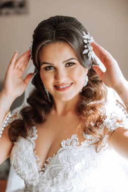 Şık bir gelinlik içinde siyah saçlı ve düğün sabahı odasında çarpıcı makyajlı güzel bir gelinin moda fotoğrafı. Gelin düğün için hazırlanıyor.