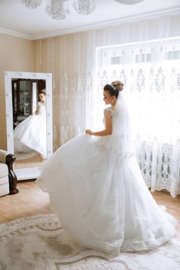 Uzun gelinlik ve duvak giymiş genç esmer otel odasında. Büyüleyici bir gelin, uzun boylu, muhteşem beyaz elbisesiyle düğünden önceki sabah.