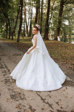 Uzun trenli beyaz elbiseli esmer bir gelin elbiseyi tutar ve taş patikadan aşağı doğru yürür. Sonbahar. Doğada düğün fotoğrafı çekimi. Güzel saç ve makyaj. kutlama