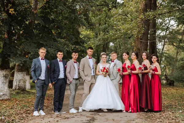 Wedding photo session in nature. The bride and groom and their friends pose against the background of trees. Happiness. A group of young people. Celebration. Autumn wedding. The same clothes