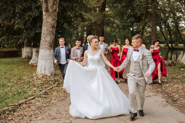 Wedding photo session in nature. The bride and groom and their friends are walking in the forest. Happiness. A group of young people. Celebration. Autumn wedding. The same clothes