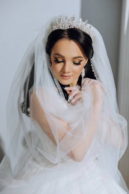 Şık bir gelinlik içinde siyah saçlı ve düğün sabahı odasında çarpıcı makyajlı güzel bir gelinin moda fotoğrafı. Gelin düğün için hazırlanıyor.