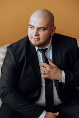 Beyaz gömlekli genç bir adam odanın penceresinin yanında duruyor ve kravat takıyor. Damat sabah giyinir ve düğün için hazırlanır..