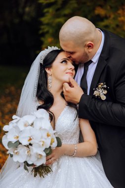 Genç bir gelin ve damat sonbahar güneşinin ışınlarında şefkatle kucaklaşır. Şefkatli ve güzel genç kız gelin. Bir adam sevgilisini öper. Güzel bir bahçenin arka planında