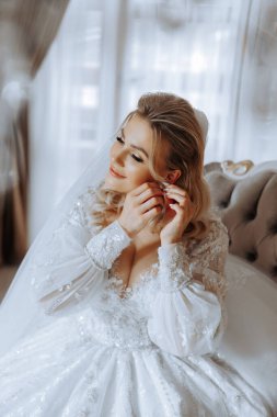 Evdeki düğün töreninden önce küpe takan genç ve güzel bir gelin. Beyaz gelinlikli bir gelin, sabahları odasına küpe takar..