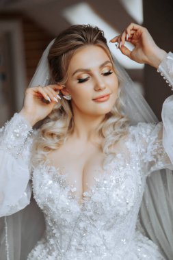 Şık bir gelinlik içinde siyah saçlı ve düğün sabahı odasında çarpıcı makyajlı güzel bir gelinin moda fotoğrafı. Gelin düğün için hazırlanıyor.