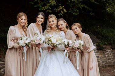 Düğün fotoğrafçılığı. Beyaz elbiseli, buketi olan sarışın bir gelin ve krem rengi elbiseli esmer arkadaşları ormanda poz veriyorlar. Sonbahar düğünü. Arkadaşlık. Bir grup genç kız. Kutlama.