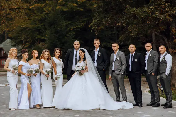 Wedding photo session in nature. The bride and groom and their friends pose against the background of trees. Happiness. A group of young people. Celebration. Autumn wedding. The same clothes