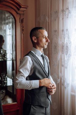 Düğünden önce ceketinin düğmelerini ilikleyen genç bir adam. Takım elbiseli bir adamın yakın çekimi. İş adamı takım elbise giyer. Bir adam ceketinin düğmelerini bağlar..