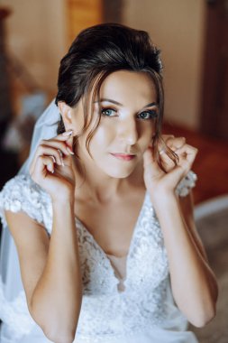 Evdeki düğün töreninden önce küpe takan genç ve güzel bir gelin. Beyaz gelinlikli bir gelin, sabahları odasına küpe takar..