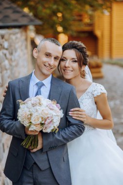 Güzel ve şık yeni evliler güzel bir bahçede sonbahar doğasının arka planına karşı sarılıp gülümsüyorlar. İnanılmaz güzel genç bir gelin, sevgili damadının omzuna yaslandı.