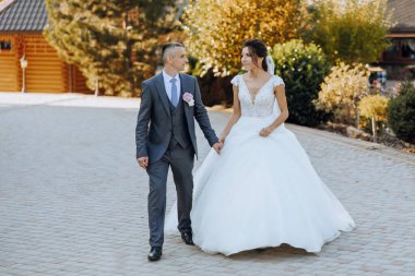 Bir düğün çifti bir sonbahar günü doğada yürüyor. Mutlu genç gelin ve zarif damat el ele tutuşuyor. Yeni evlilerin düğün gününde şık bir çift..