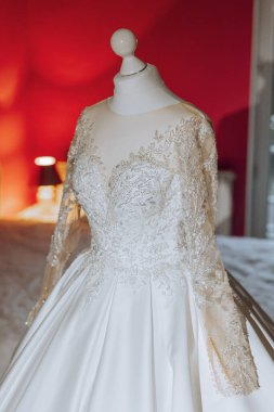 Yatak odasının içinde tören için hazırlanmış gelinlik var. Bir otel odasında, bir mankenin üzerinde güzel, gür bir gelinlik..