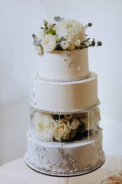 Ziyafet salonunda büyük lüks, çok katmanlı bir düğün pastası taze beyaz gül çiçekleriyle süslenir. Akşam ışığında düğün tatlısı. Düğün dekoru.