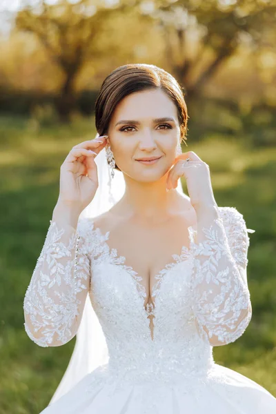Wedding portrait. A brunette bride in a lace dress with open shoulders poses in nature. Beautiful hair and makeup. Autumn. Daylight. celebration.