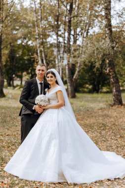 Sonbahar parkında yürüyüş yapan düğün çifti. Güzel beyaz elbiseli gelin. Aşk ve ilişki kavramı. Doğada damat ve gelin