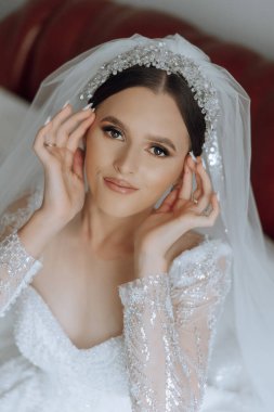 Şık bir gelinlik içinde siyah saçlı ve düğün sabahı odasında çarpıcı makyajlı güzel bir gelinin moda fotoğrafı. Gelin düğün için hazırlanıyor.