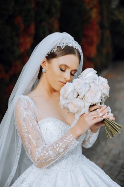 Portre. Elbise ve peçeli esmer bir gelin, şık bir tacı var, poz veriyor ve onun buketini kokluyor. Gümüş mücevherler. Güzel makyaj ve saç. Sonbahar düğünü. kutlama
