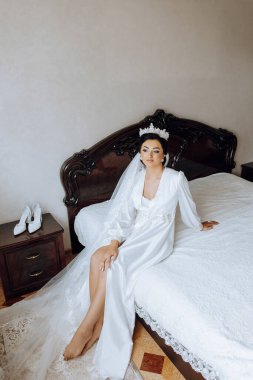 Sabahları beyaz bir bornozla inanılmaz güzel bir gelin ve yatak odasındaki yatakta uzun bir peçe oturuyor. Gelin, düğün töreninden önce poz verir..