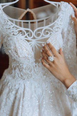 Gelin gelinliğine dokunuyor. Yüksek kalite fotoğraf. Beyaz etekli güzel bir gelin yatağın yanında duruyor, gelinliğine dokunuyor..