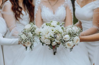 Düğün fotoğrafçılığı. Beyaz elbiseli, buketli esmer bir gelin ve krem rengi elbiseli esmer arkadaşları bahçede poz veriyor. Arkadaşlık. Bir grup genç kız. kutlama.
