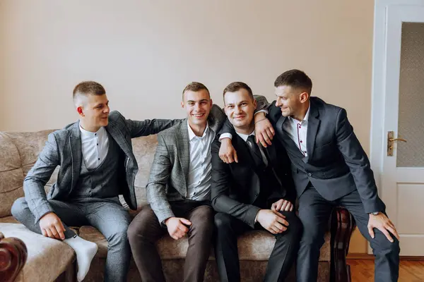 A young groom and his funny friends pose for the camera. A group of young people hug the groom and cheerfully congratulate him. Happy friends. Friends in the room. Wedding day.