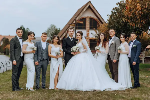 Wedding photo session in nature. The bride and groom and their friends pose against the background of the house. Happiness. A group of young people. Celebration. Autumn wedding. The same clothes