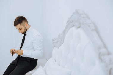 Pencere kenarındaki bir adam ayarlar ve deri kemerli bir kol saati takar, beyaz gömlek giyer ve altın bir yüzük takar..